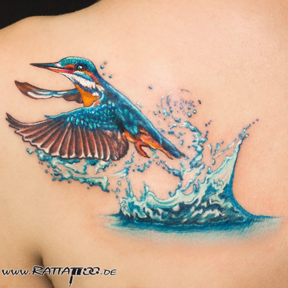 Aus dem Wasser aufsteigender Eisvogel in Farbe auf der Schulter aus dem Rattattoo Tattoostudio in Freiburg.